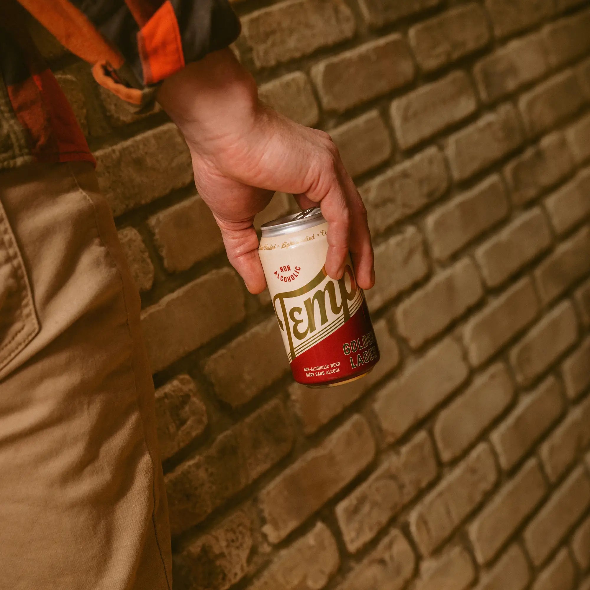 Man holding a can of Templ beer against a brick background