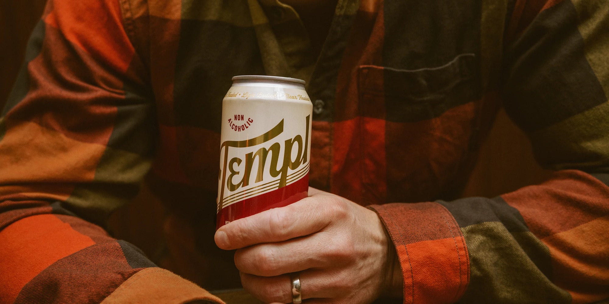 Man wearing a red plaid shirt holding a Templ can